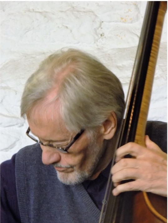 Photograph of Finnish composer Teppo Hauta-aho with his double bass, looking away from the camera.