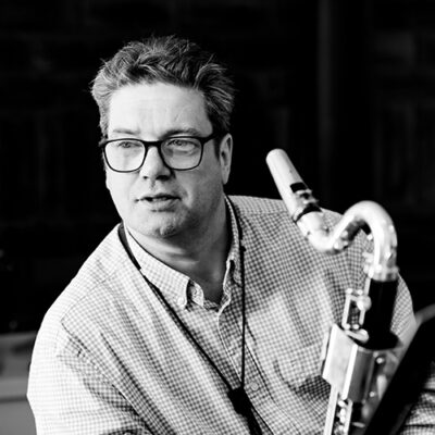 Black and white photograph of composer and musician Paul Saunders holding a saxophone.